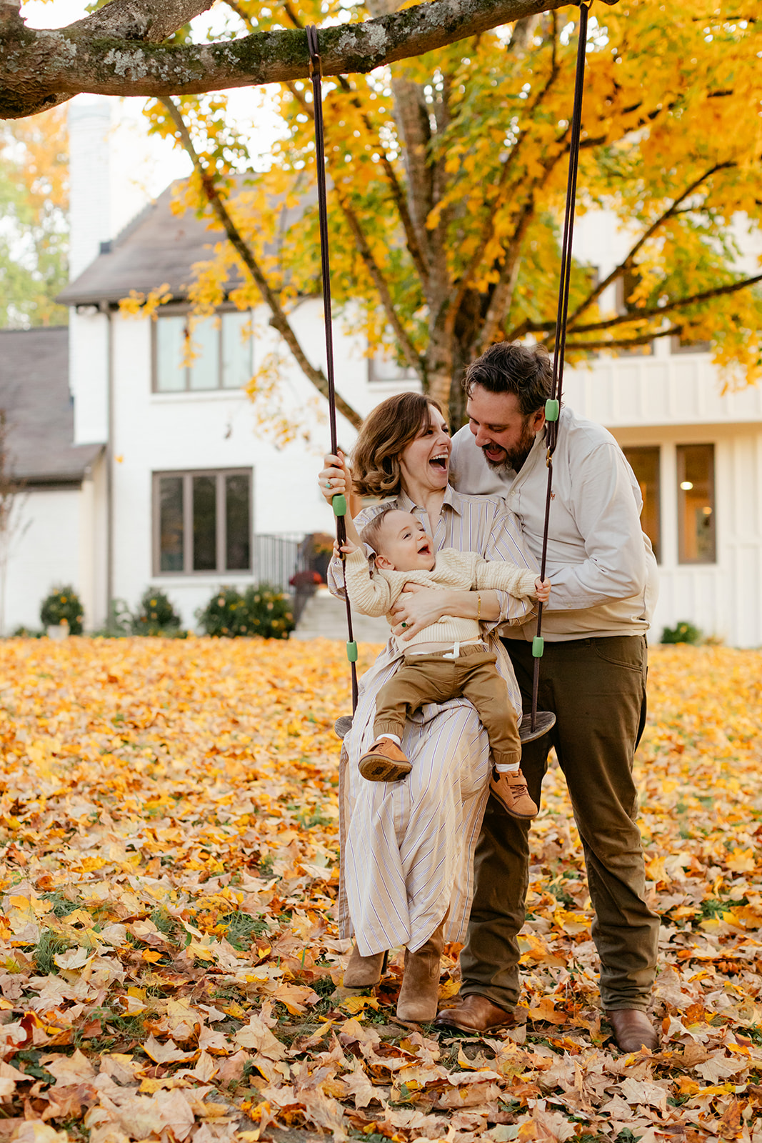outdoor fall family session. mama sitting with son on swing and dad behind