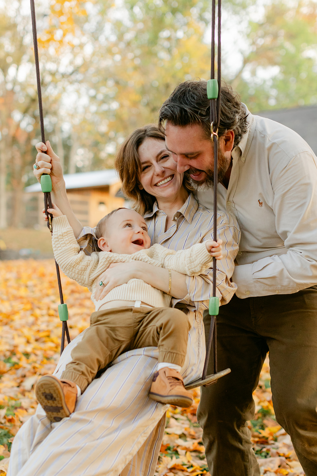 outdoor fall family session. mama sitting with son on swing and dad behind