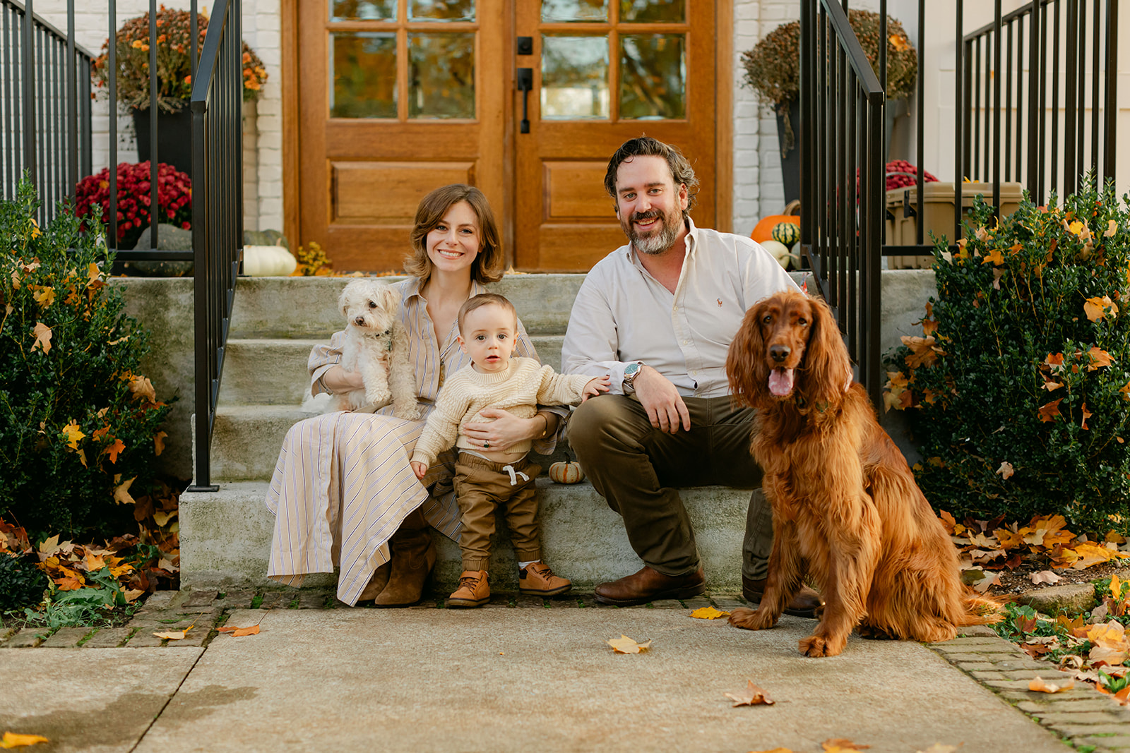 outdoor fall family session. parents and baby boy sitting in front porch with their two dogs